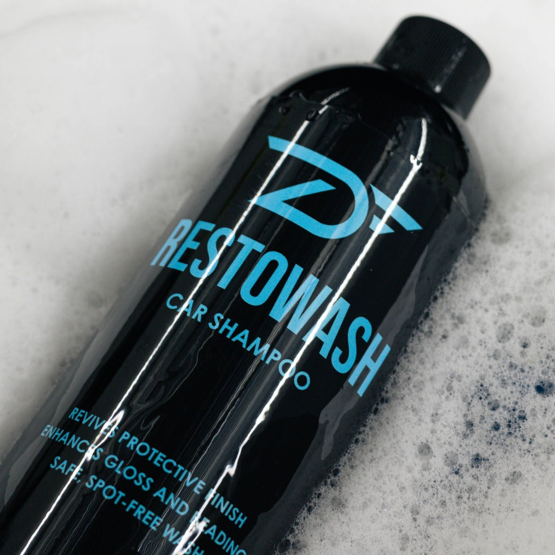 Black bottle of Restowash car shampoo with blue text on a soapy background