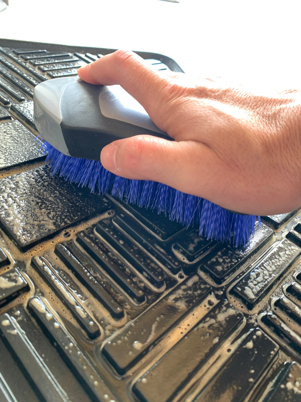 Using an upholstery brush to agitate and remove dirt from rubber floor mat